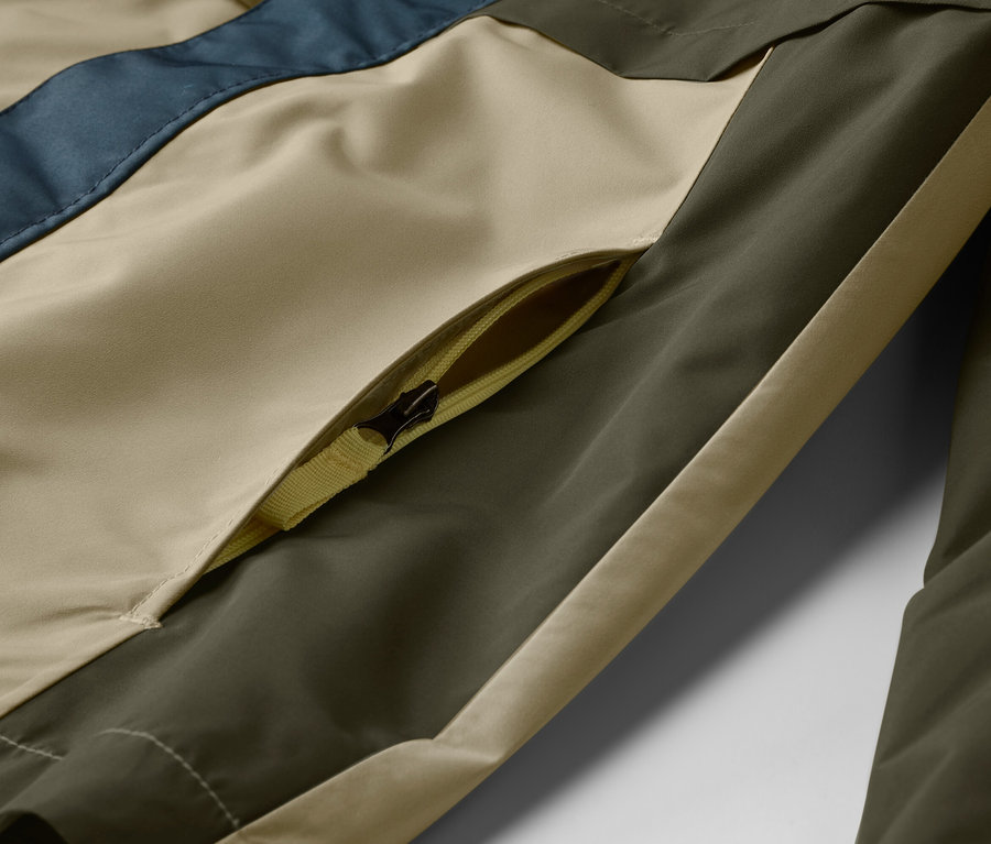 Detail bundy s kapsou na zip v béžové, olivově zelené a modré barvě.