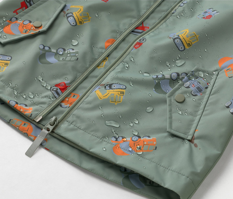 Detailní záběr olivově zelené bundy se zipem a motivem staveniště, pokryté kapkami vody.