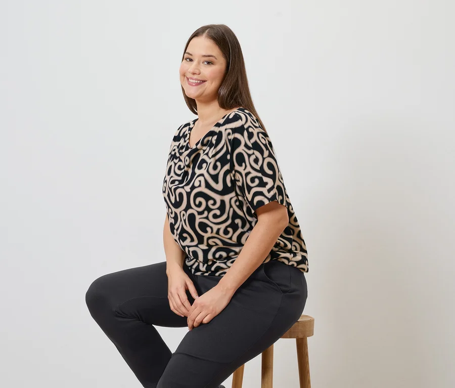 Žena sedí na stoličce a má na sobě vzorovanou blůzu a kalhoty joggpant.
