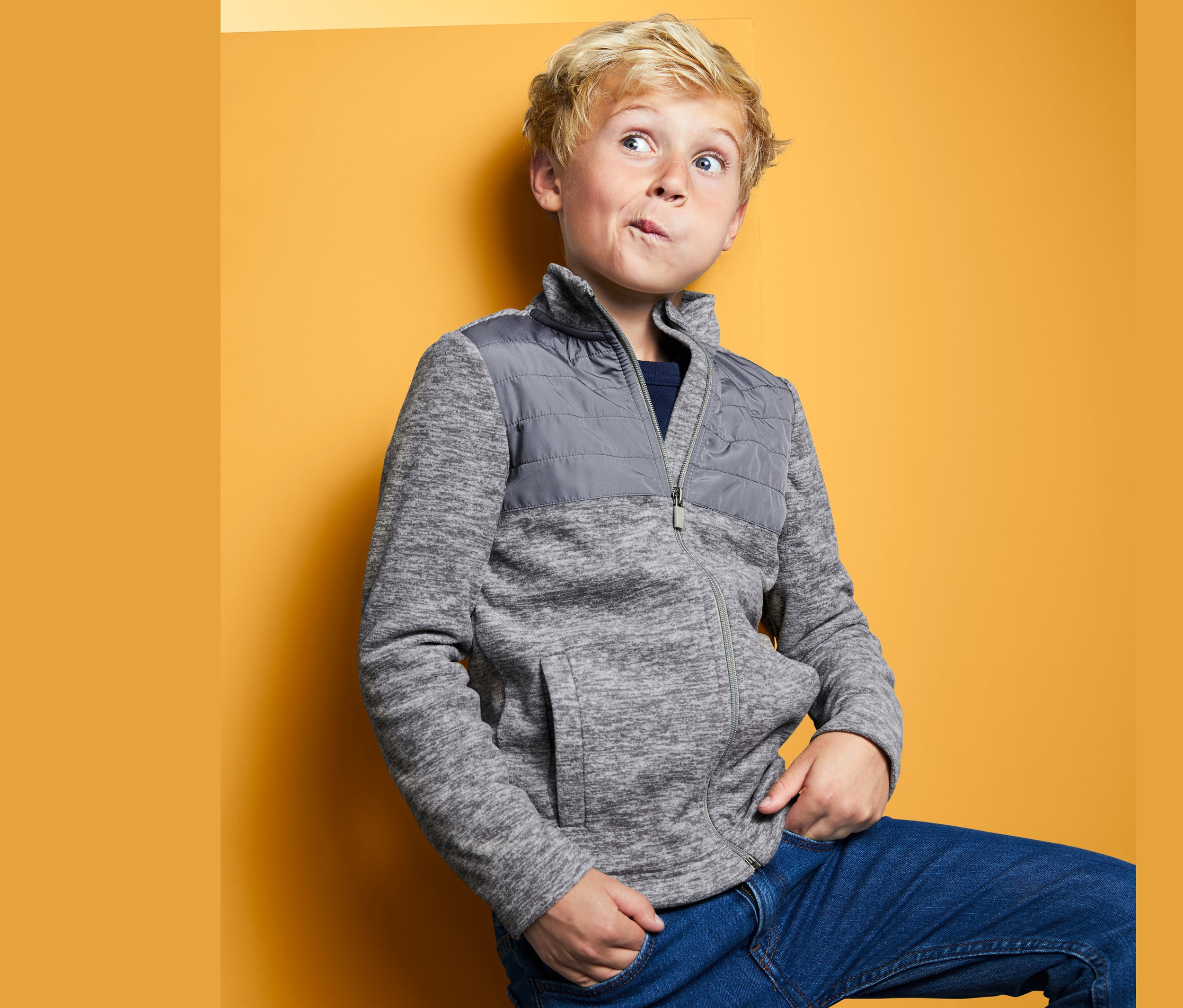 Chlapec pózuje v hybridní fleecové bundě před žlutým pozadím.