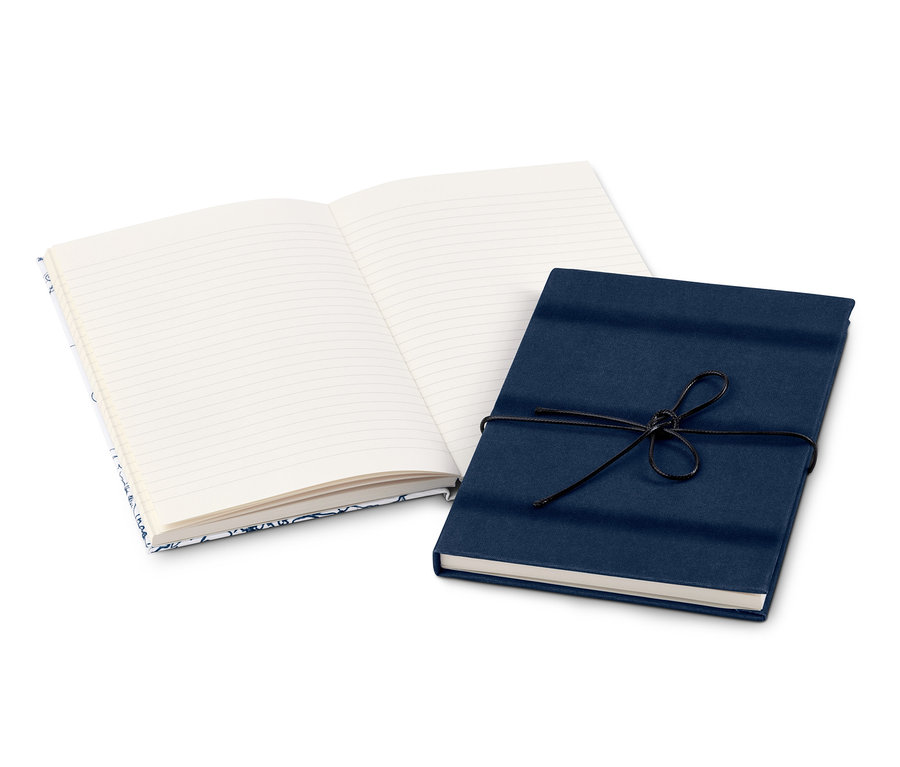Dva poznámkové bloky leží na bílém povrchu. Jeden je otevřený a má linkované stránky, druhý je zavřený a obalený tmavě modrým papírem a převázaný černou šňůrkou.