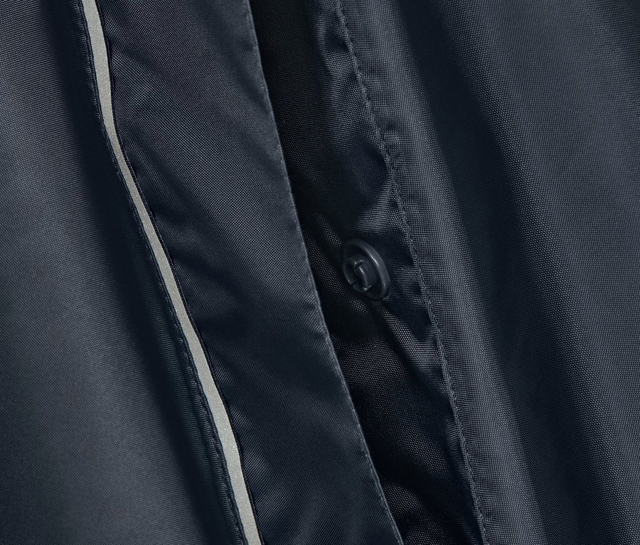 Detail modrého ponča do deště s knoflíkem a reflexním pruhem.
