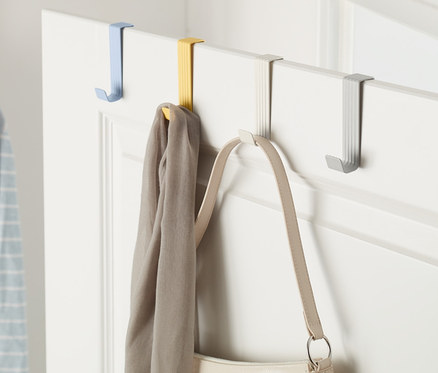 Na dveřích jsou zavěšeny 4 háčky na dveře různých barev, na kterých visí šála a kabelka.