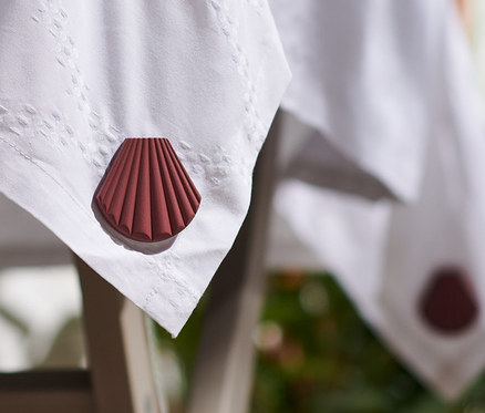 Roh stolu s bílým ubrusem je zatížen hnědým závažím na ubrus ve tvaru mušle, celkem 4 ks.