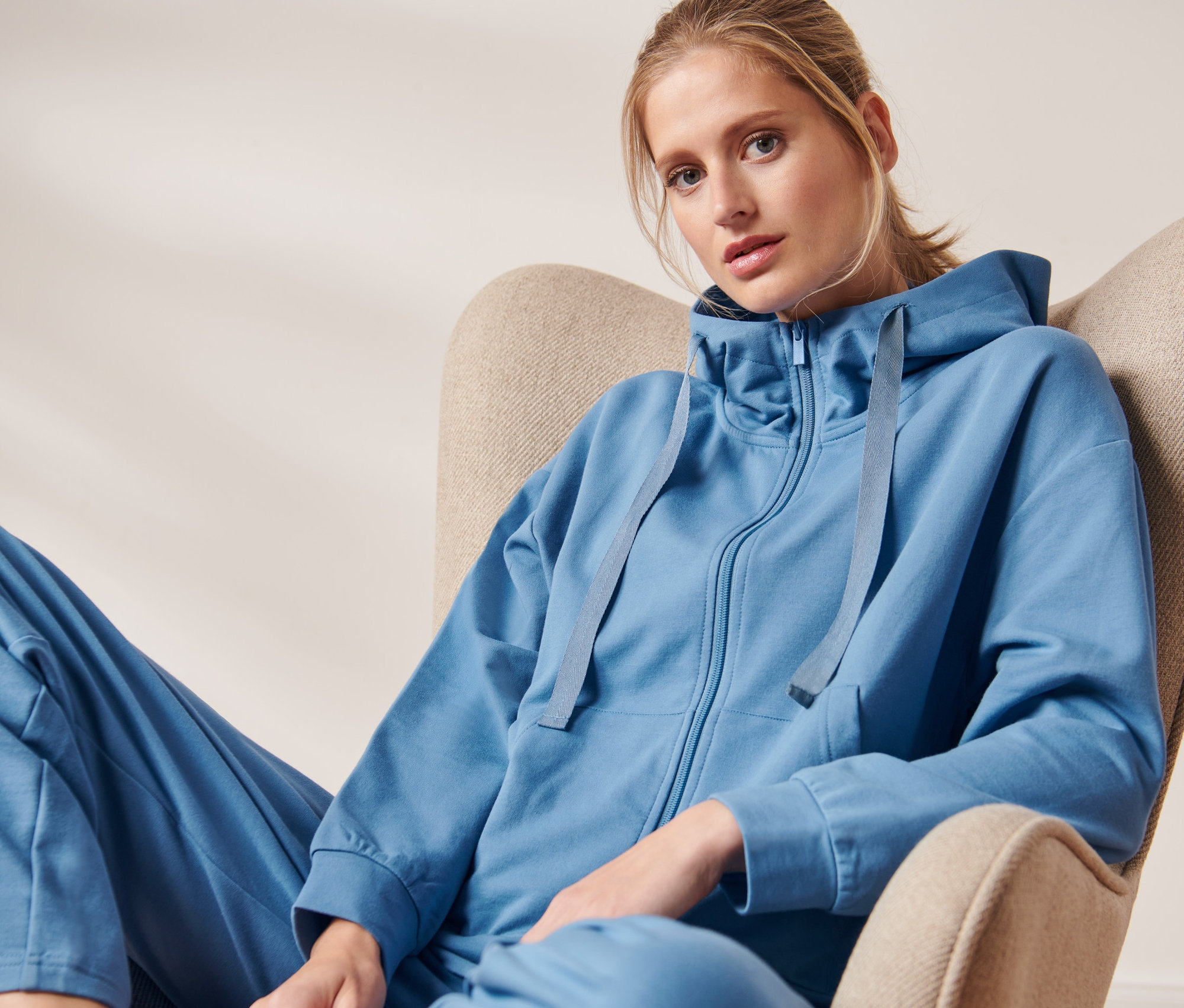 Žena sedí v křesle a má na sobě pohodlnou mikinu.