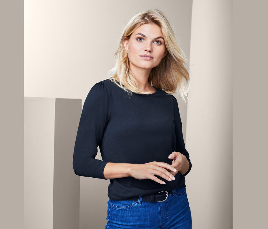 Blondýna má na sobě modré džíny a černé triko s dlouhým rukávem.