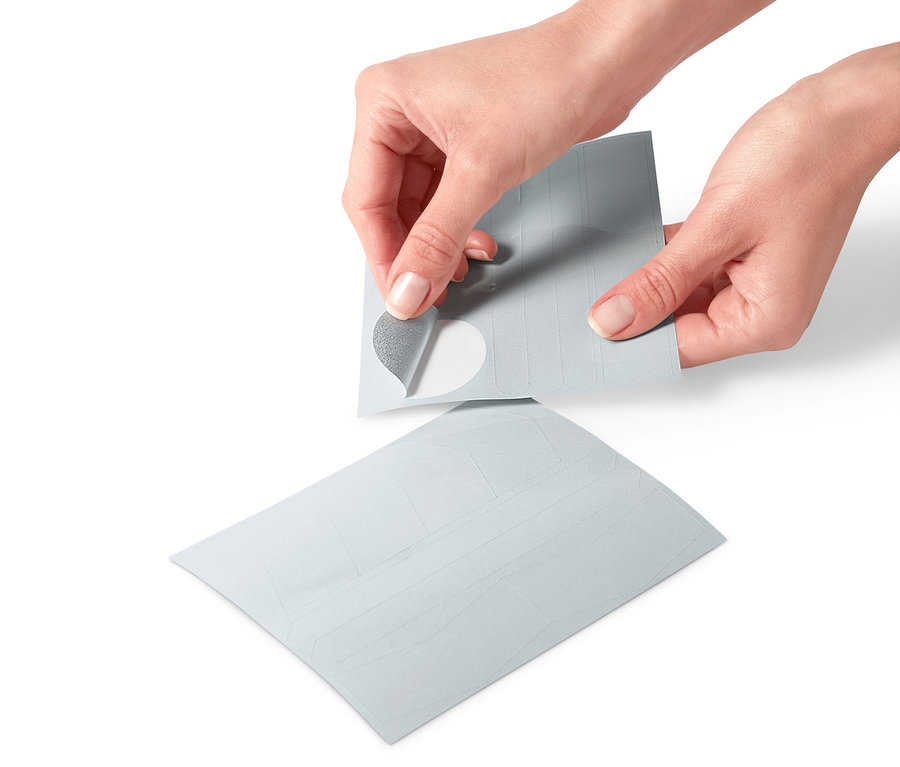 Ruce odlepují reflexní nálepku z archu reflexních samolepek, 16 ks.