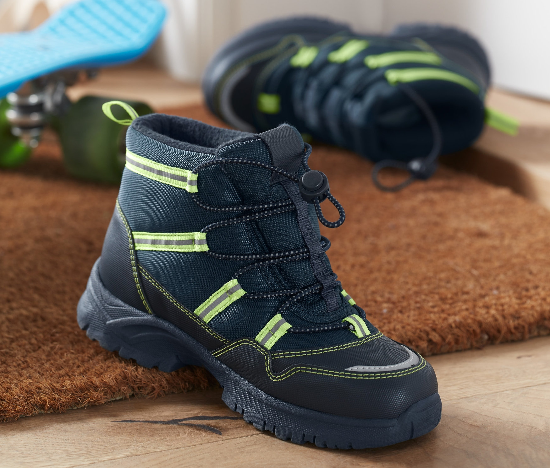 Tmavě modré kotníkové termoboty na podložce u dveří.