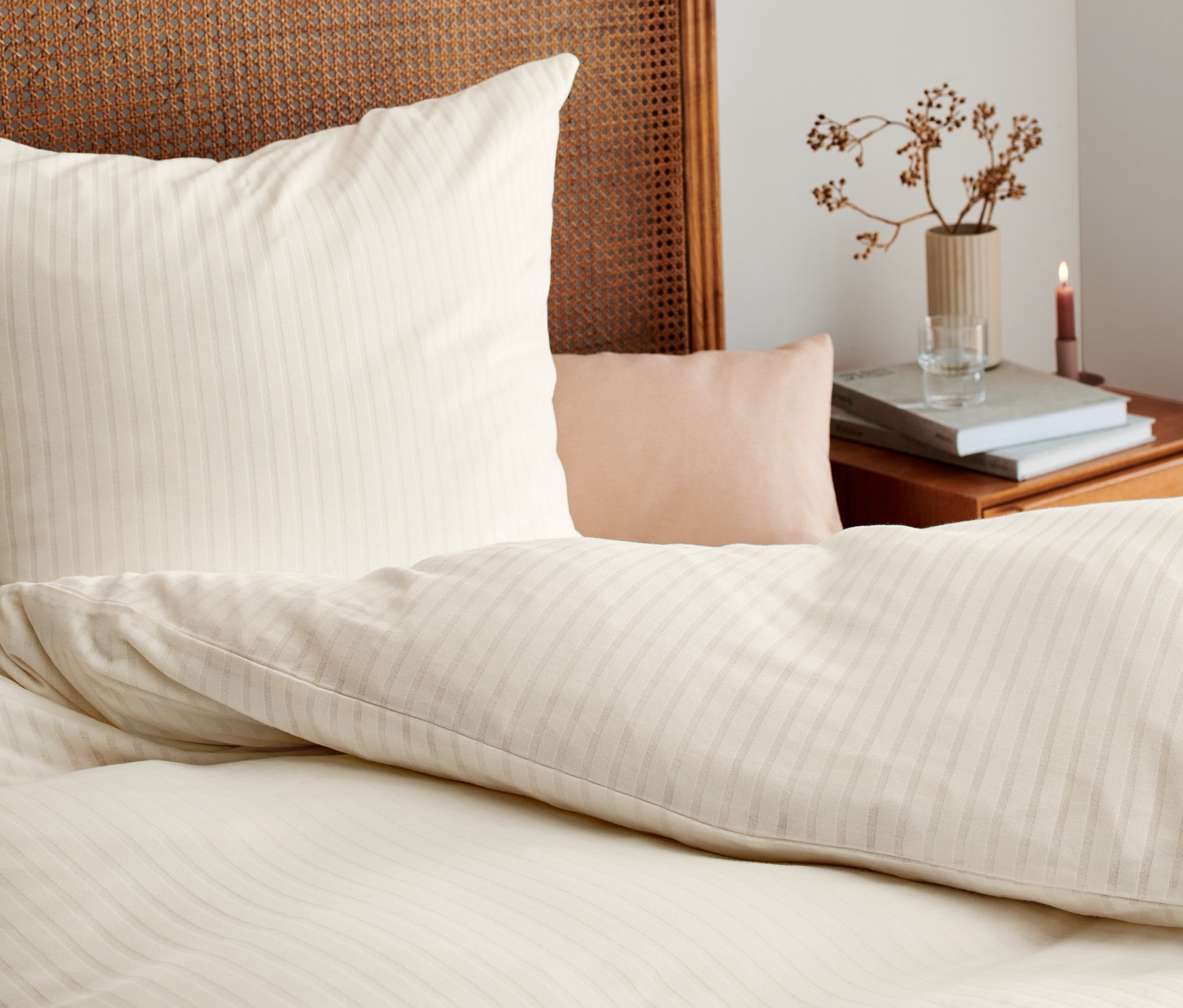 Detail béžového žerzejového povlečení na posteli s proutěným čelem postele.