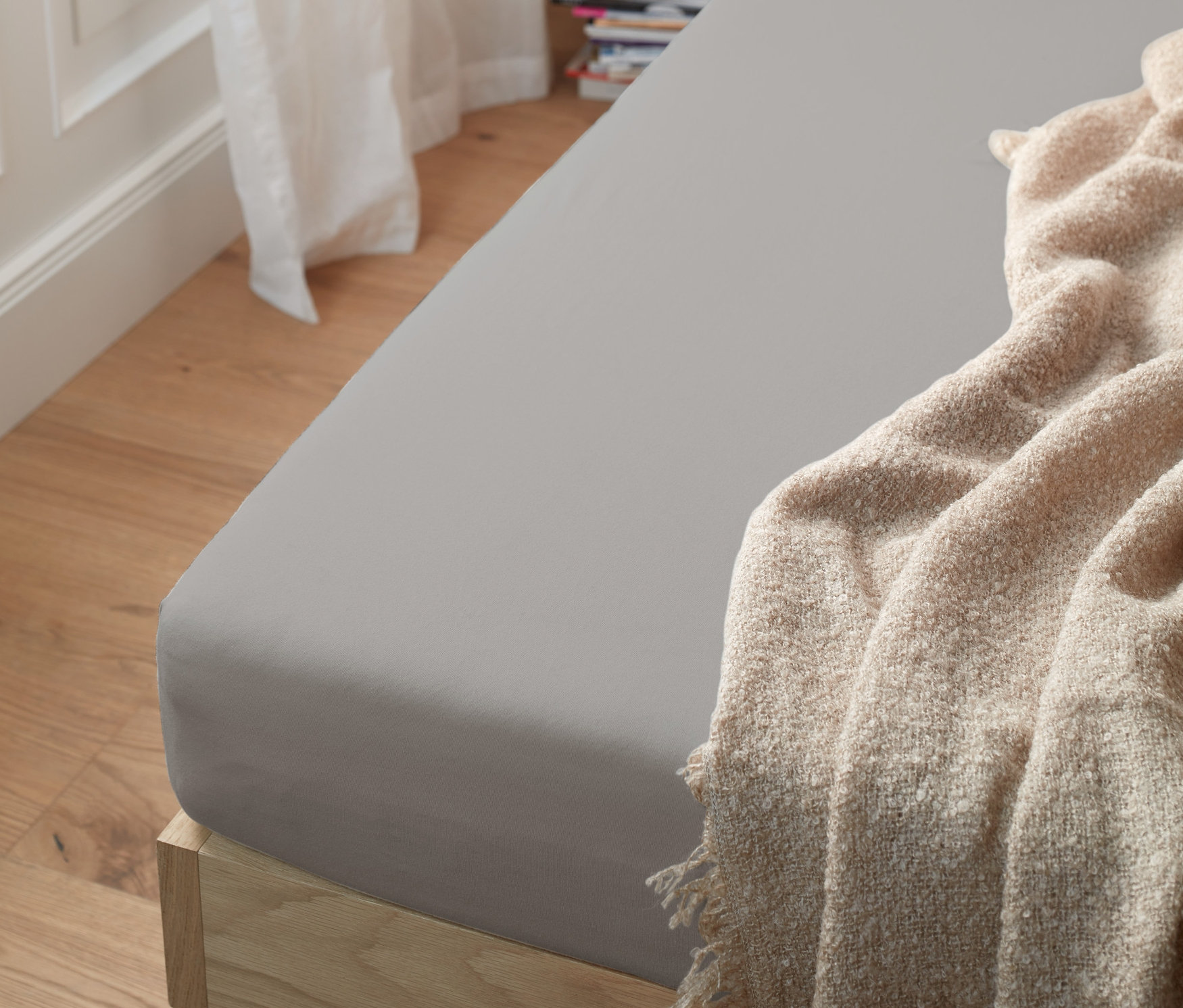 Šedé žerzejové napínací prostěradlo standardní velikosti na posteli s béžovou dekou.