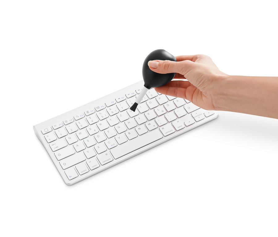 Ruka čistí bílou klávesnici pomocí Štětečku s balonkem na čištění proudem vzduchu.