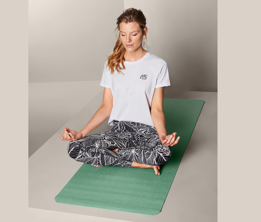 Žena sedí v tureckém sedu na podložce na jógu a na cvičení.
