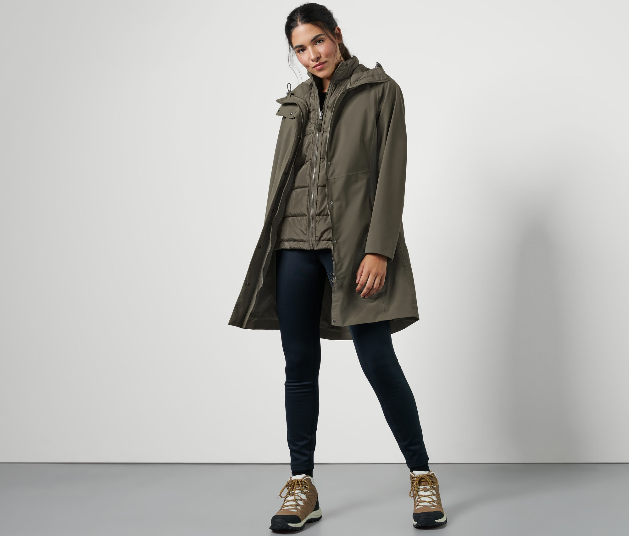 Žena pózuje v kabátě do deště s vestou 3 v 1, tmavých džínách a turistických botách.