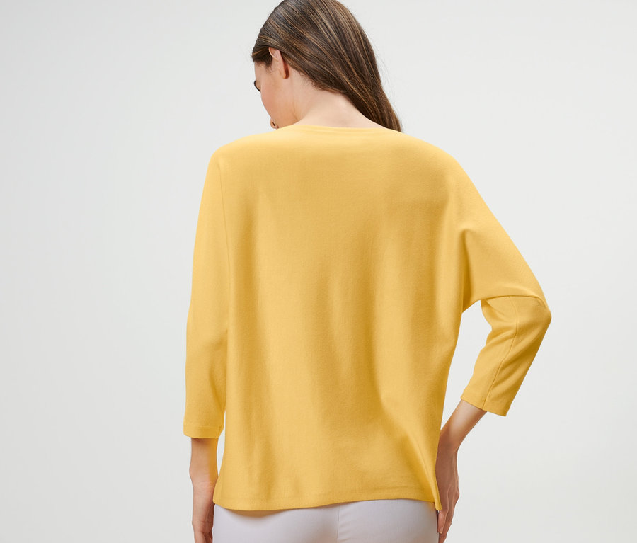 Žena má na sobě žlutý svetr z jemného úpletu.