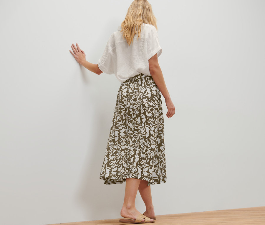 Žena pózuje v midi sukni s potiskem a bílé košili.