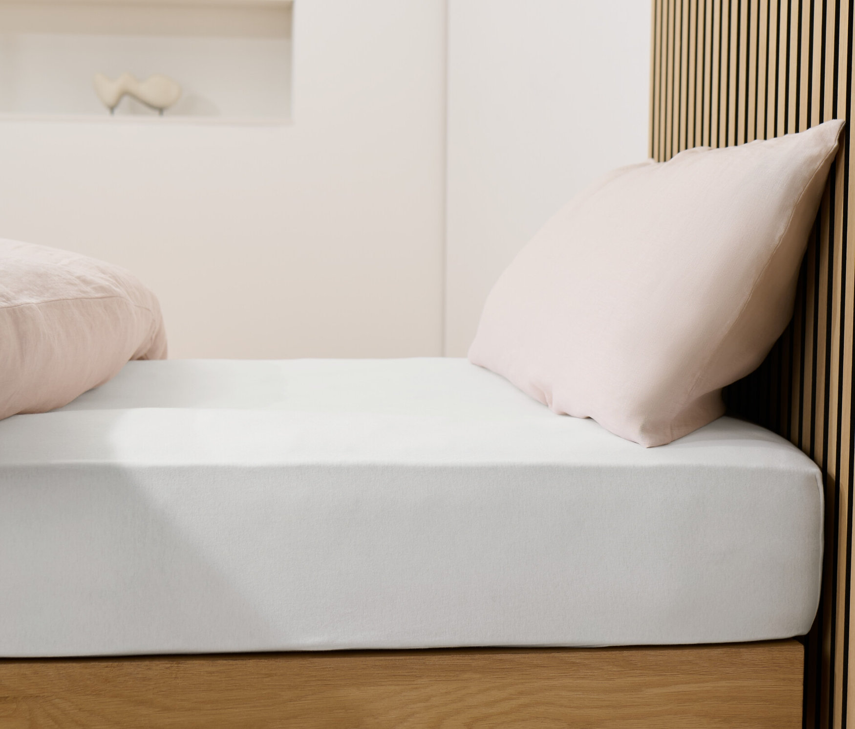 Postel s bílým žerzejovým prostěradlem a růžovými polštáři.