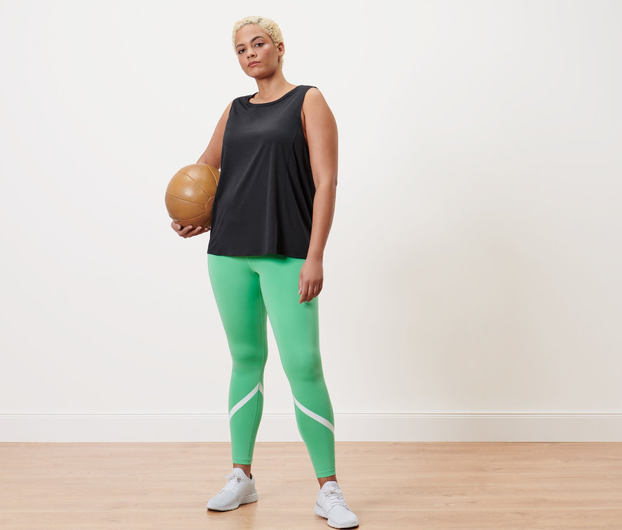 Žena drží volejbalový míč, má na sobě zelené sportovní legíny a antracitový sportovní top.