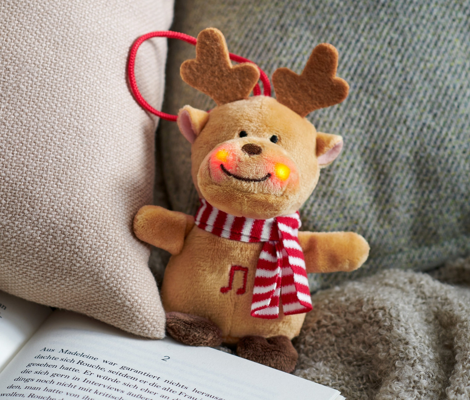 Zpívající plyšové zvířátko jelen leží na otevřené knize vedle béžového polštáře.