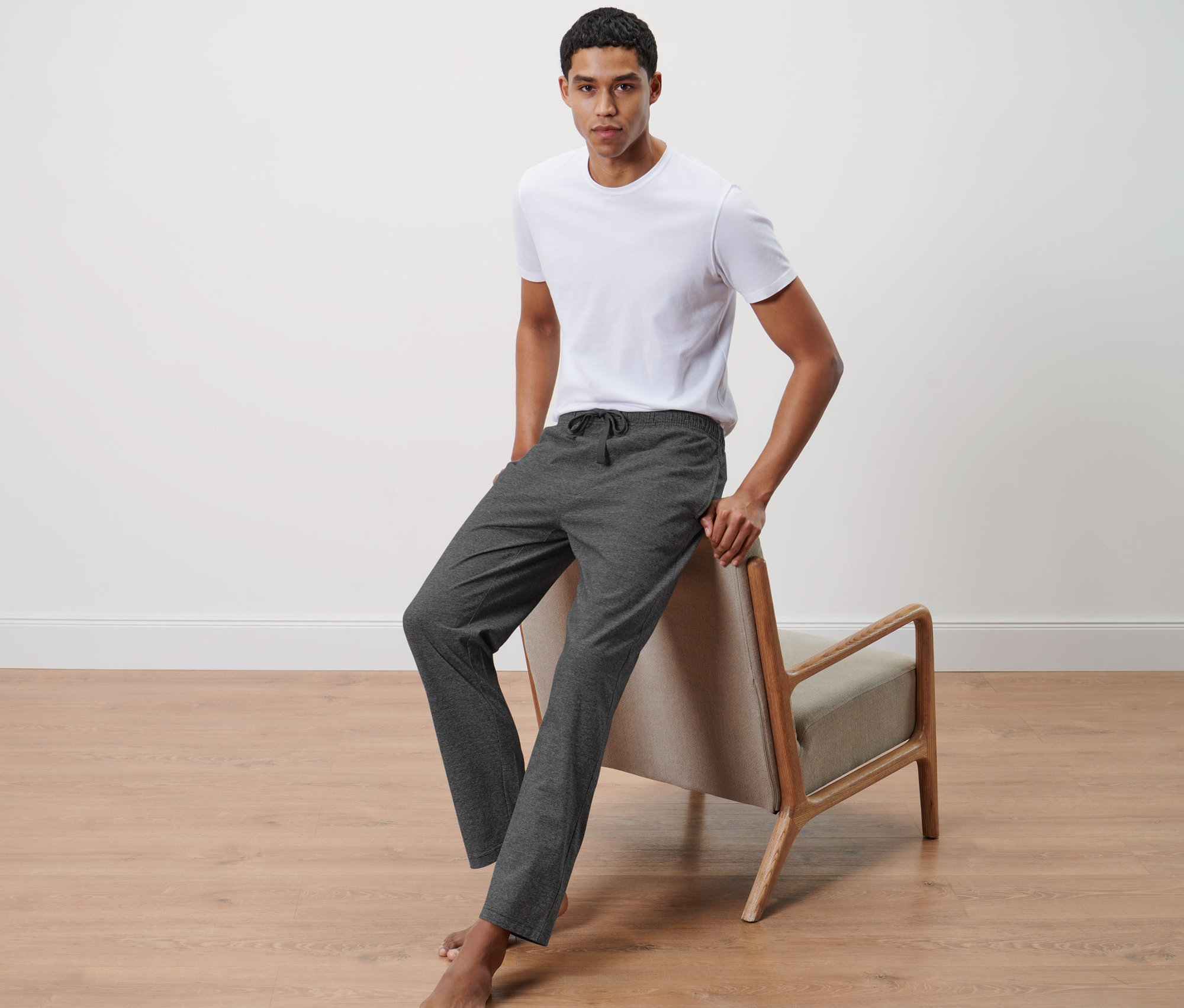 Muž opřený o židli má na sobě bílé tričko a pohodlné kalhoty.