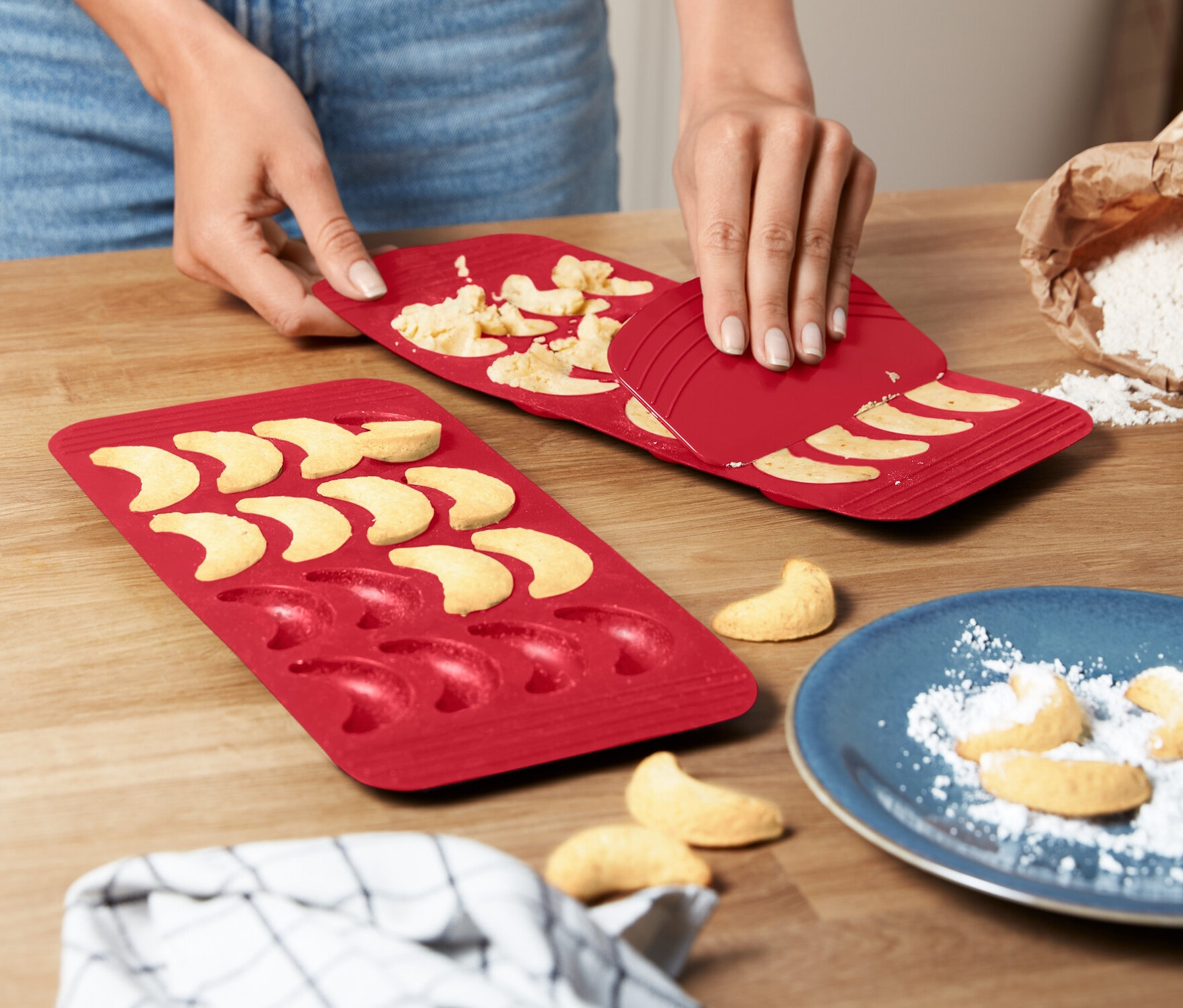 Žena vyjímá vanilkové rohlíčky z červené formy na pečení.