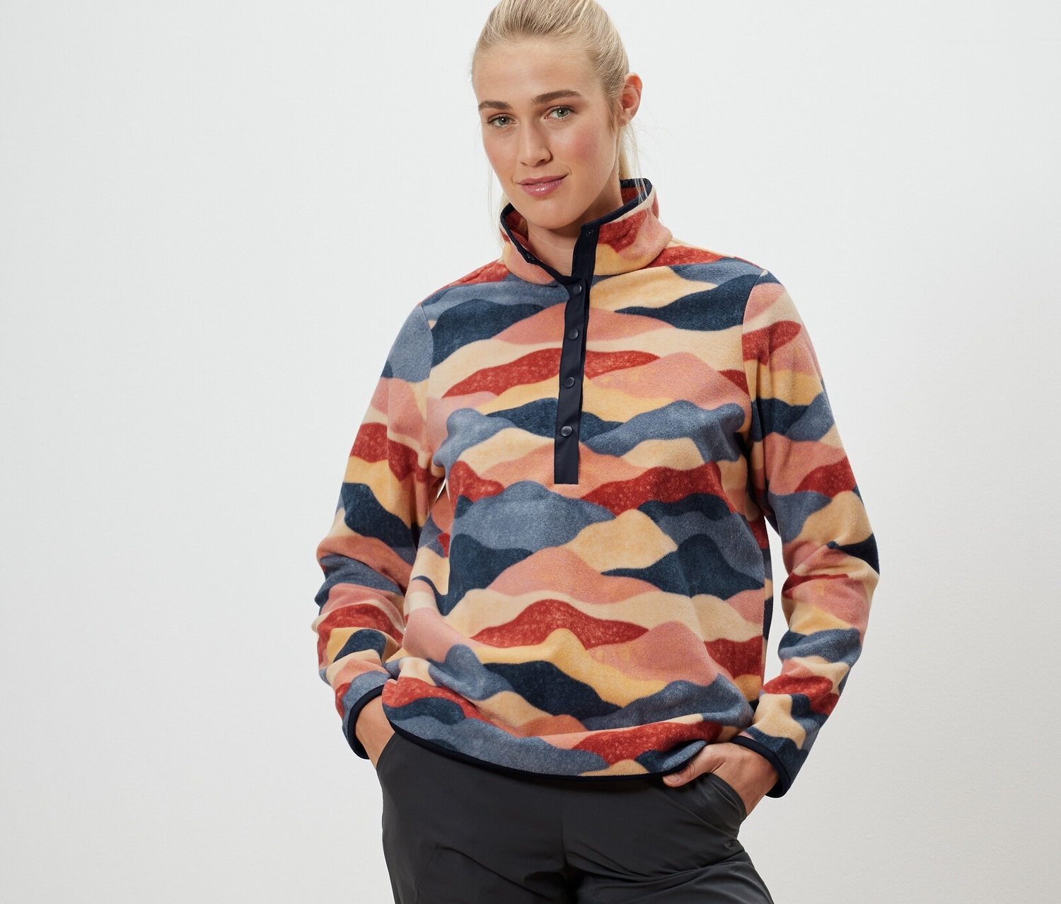 Žena stojí a má ruce v kapsách. Oblečená je do fleecové mikiny a šortek ke kolenům.