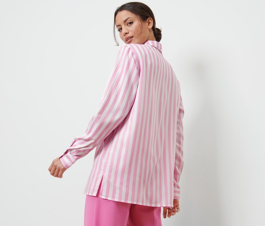 Žena se dívá přes rameno a má na sobě růžovou proužkovanou halenku.