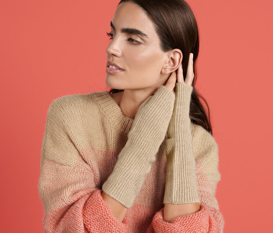 Žena se dotýká ucha, na sobě má žebrované návleky na ruce a pruhovaný svetr.