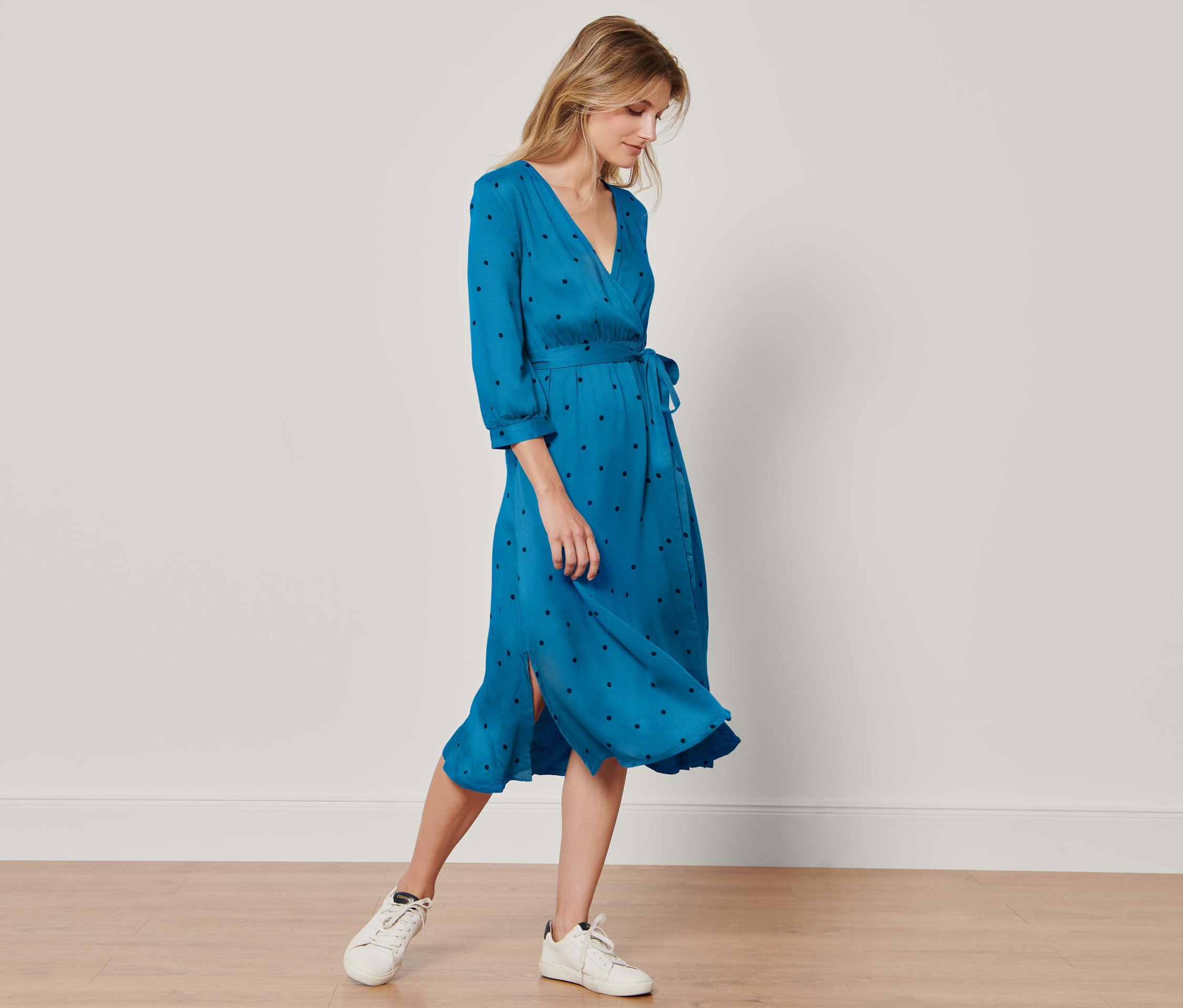 Žena stojí a má na sobě tkané šaty s puntíkovým vzorem.