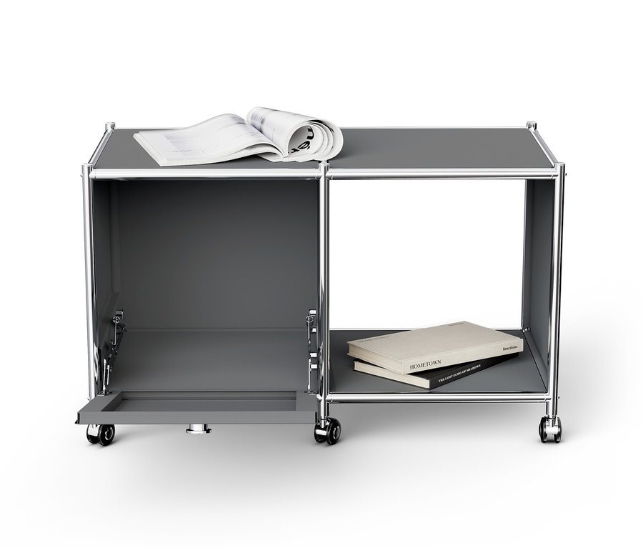 Šedý kovový odkládací stolek »CN3« s otevřeným výklopným dvířkem, knihou a časopisem.