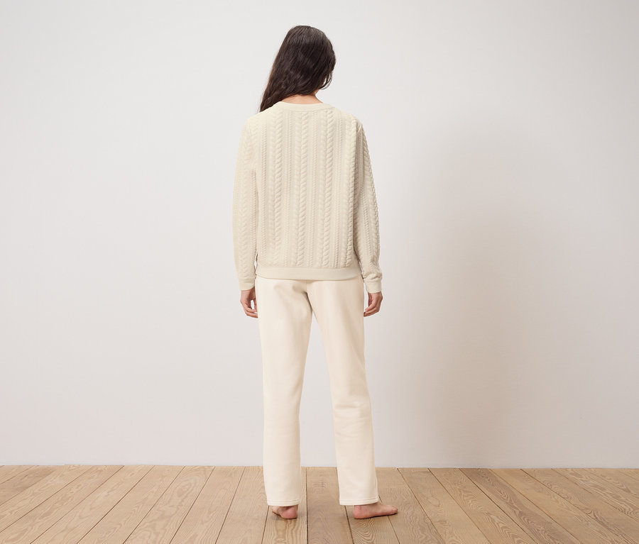 Žena stojí zády k fotoaparátu a má na sobě krémový svetr a kalhoty.