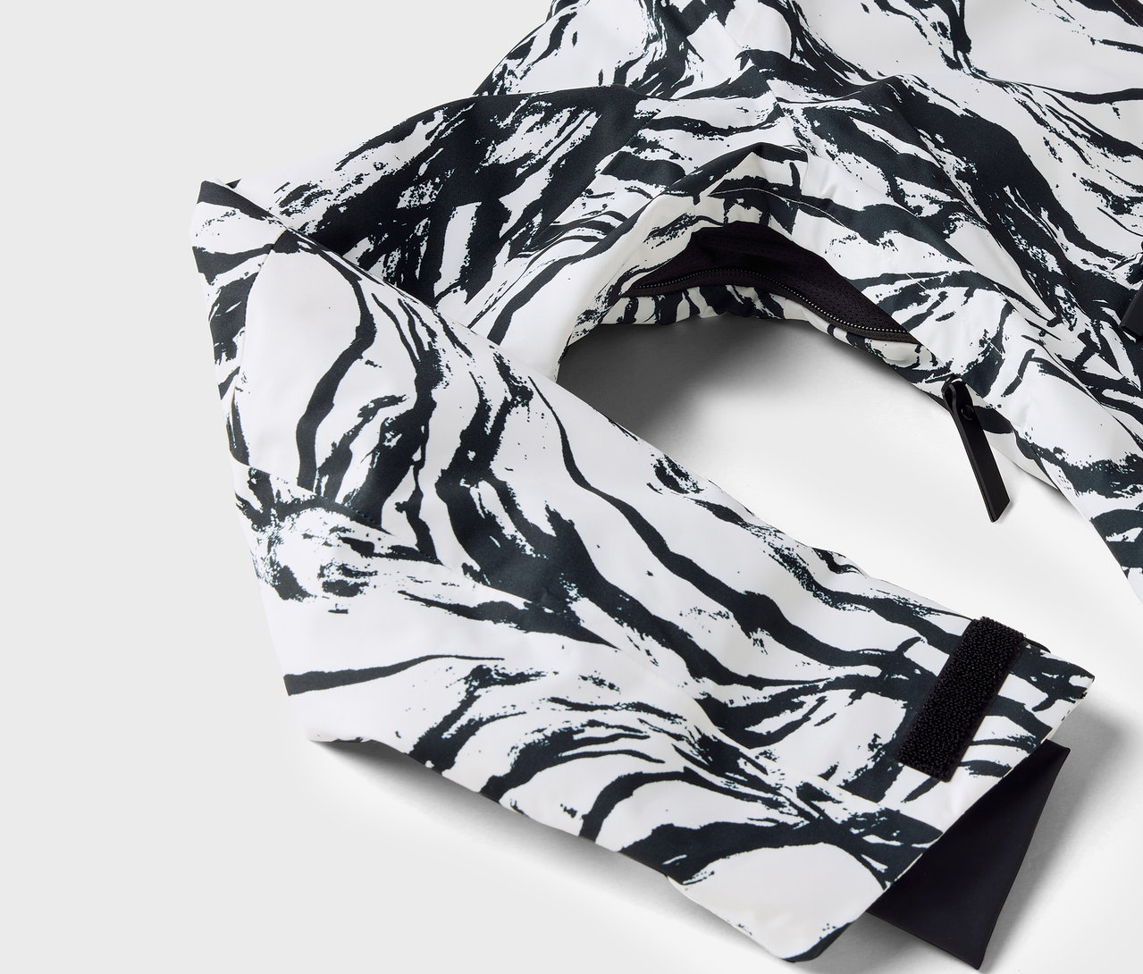 Detail bílé bundy s černým vzorem, viditelný rukáv a zip.