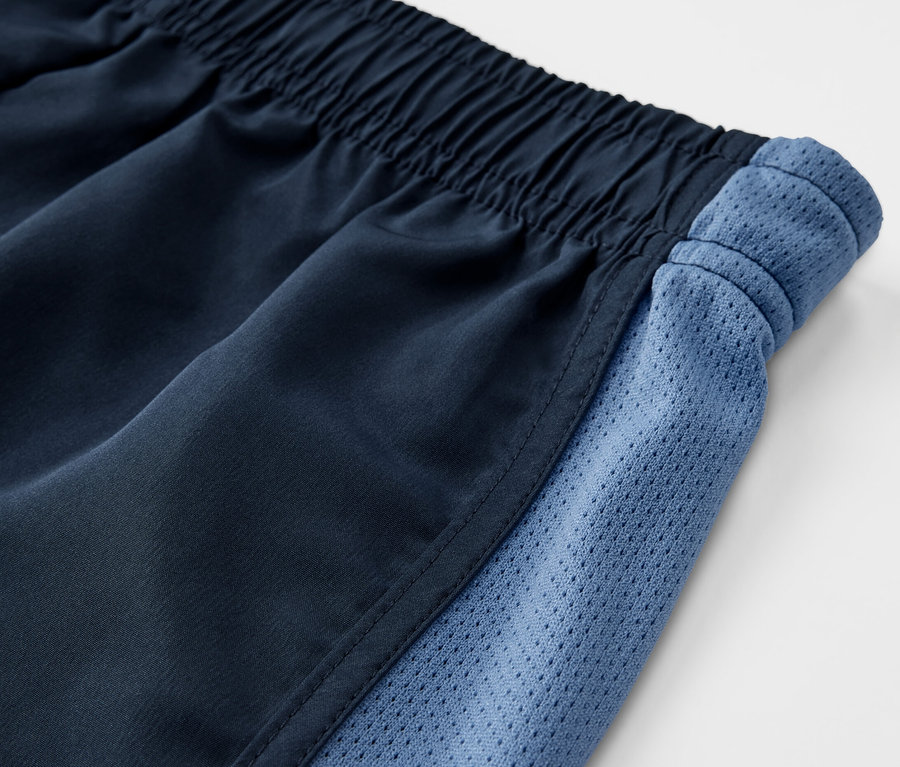 Detail dětských sportovních šortek, 2 ks, s elastickým pasem a modrými síťovanými bočními panely.