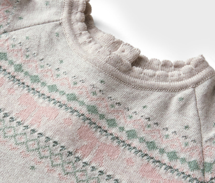 Detail svetru s růžovým a zeleným vzorem a nabíraným výstřihem.