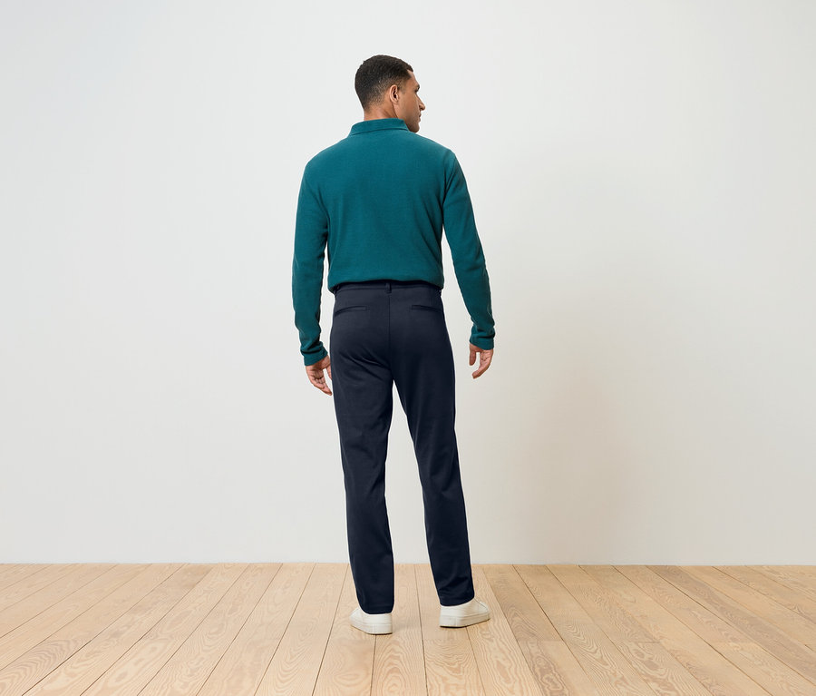 Muž otočený zády má na sobě modré kalhoty a zelený top s dlouhým rukávem.