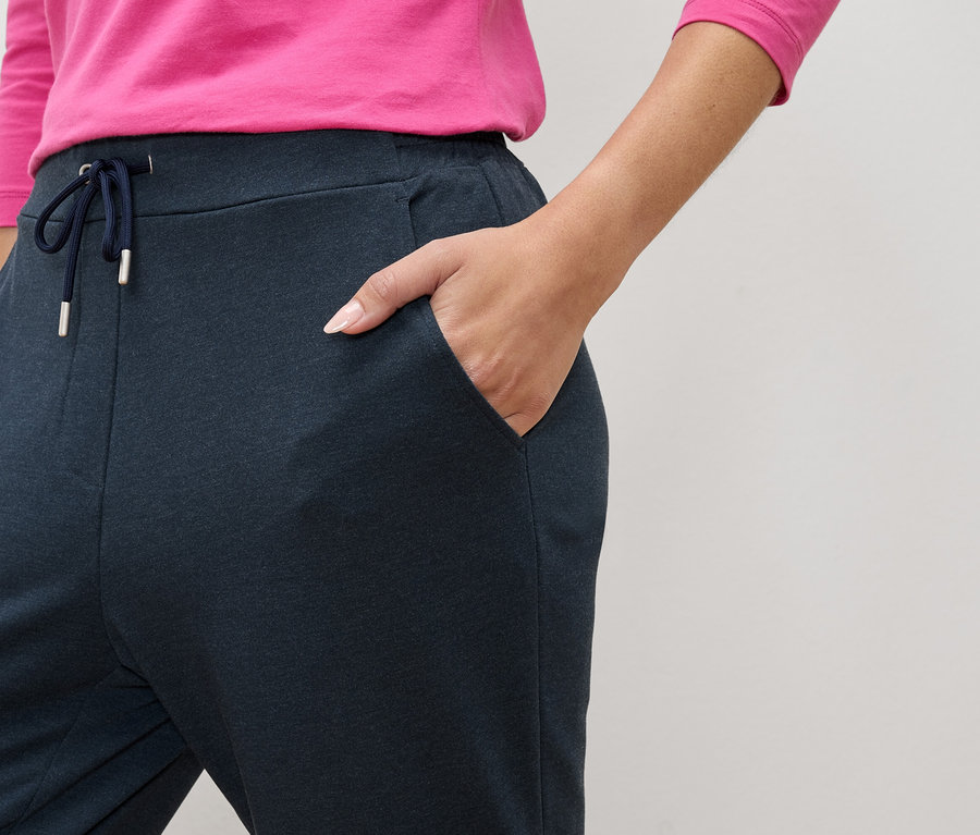 Detail osoby v tmavě modrých teplácích se stahovací šňůrkou a kapsami, s rukou v kapse.