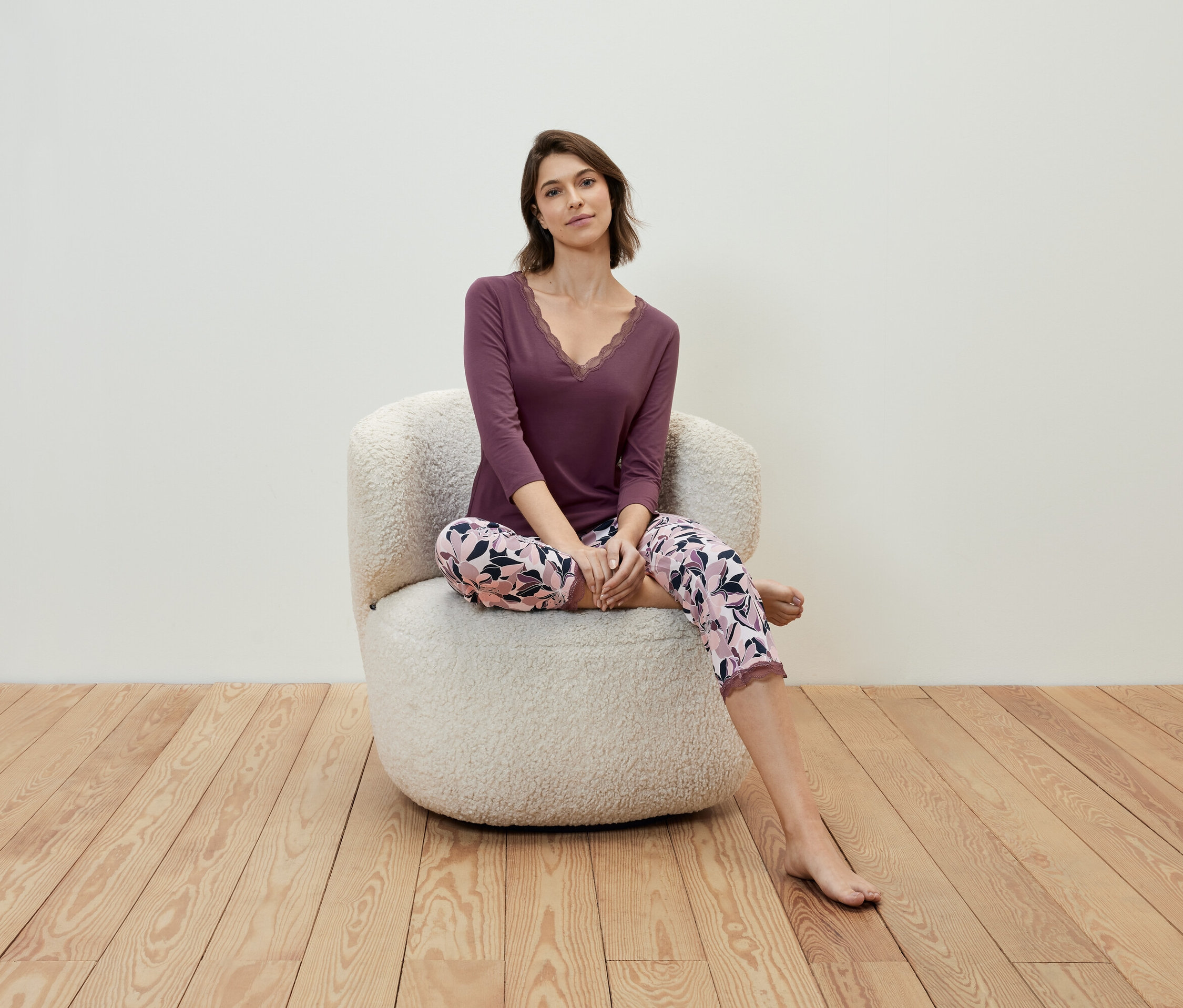 Žena sedí v křesle a má na sobě fialové tričko a květinové kalhoty.