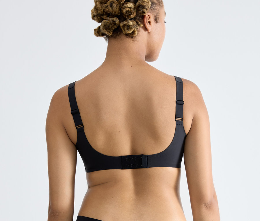 Zezadu je vidět žena s afro účesem, která má na sobě černou podprsenku sloggi ZERO Feel 2.0 Soft Bra.