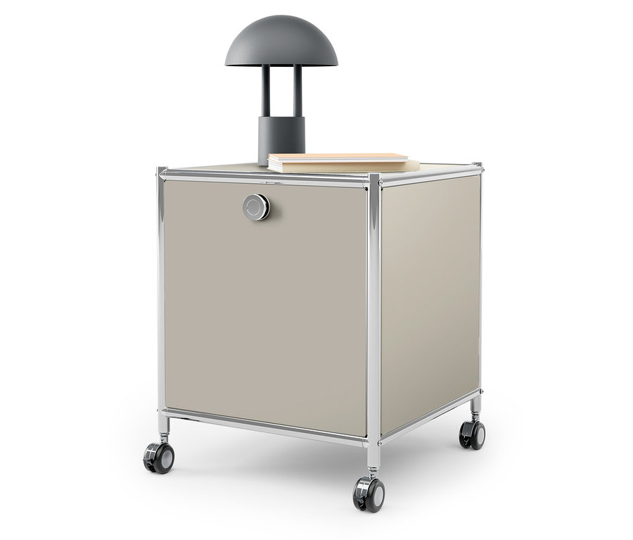 Na horní straně béžové skříňky na kolečkách stojí šedá lampa a kniha.