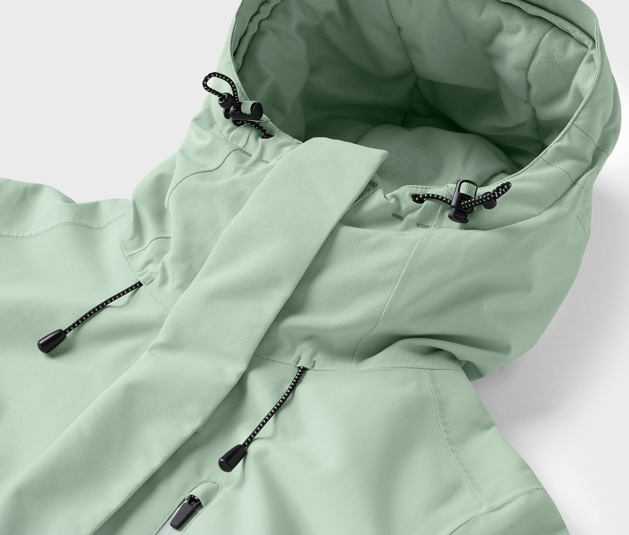 Detail světle zelené bundy s kapucí a stahovacími šňůrkami.