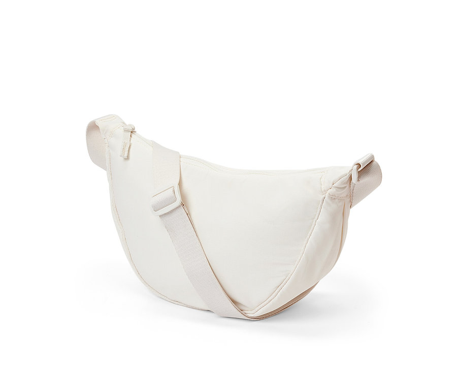 Krémová taška přes rameno leží na bílém pozadí.