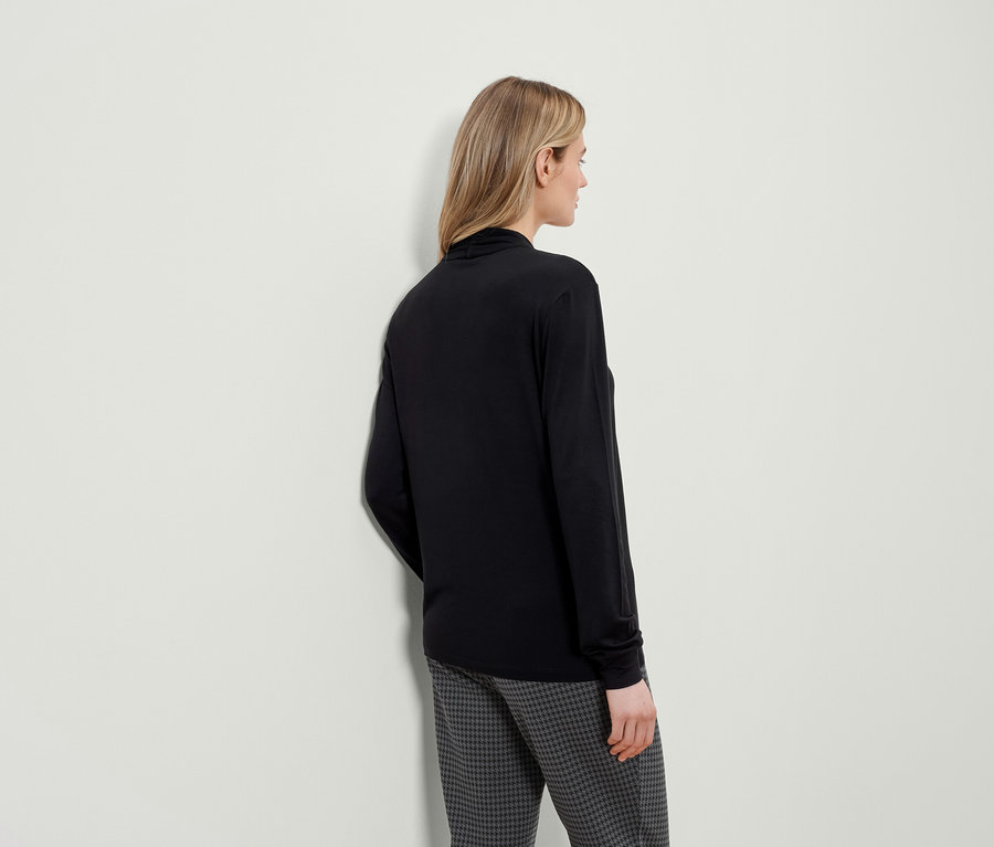 Žena zobrazená zezadu má na sobě černé tričko s dlouhým rukávem a kalhoty se vzorem houndstooth.