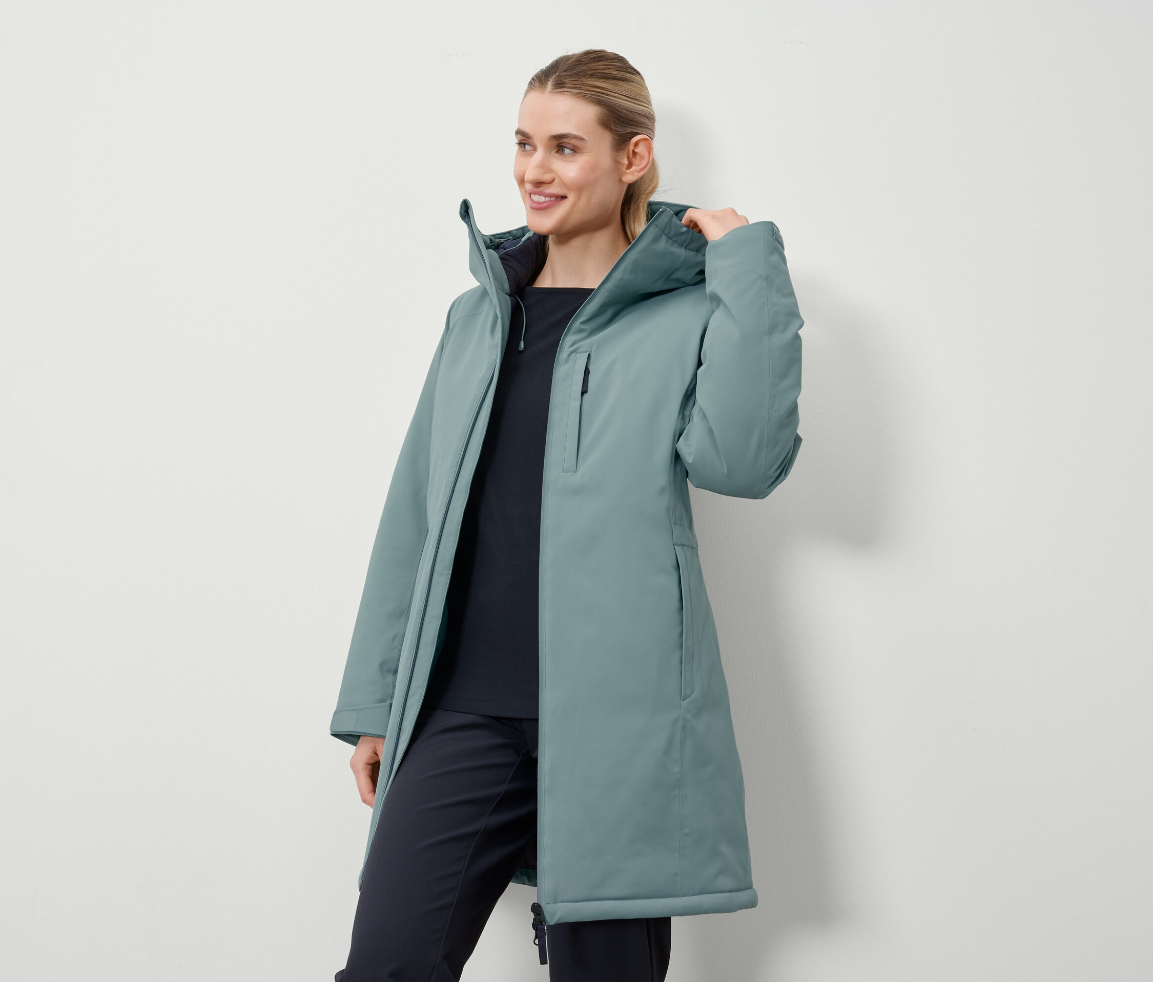 Žena má na sobě dlouhý kabát petrolejové barvy.