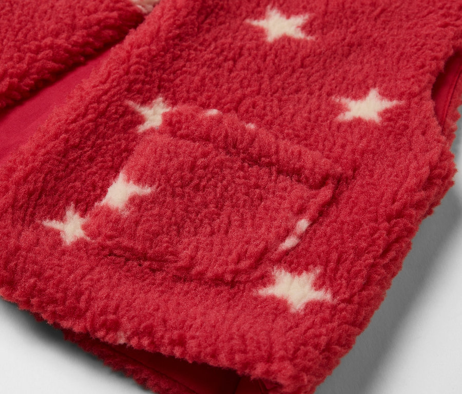 Detail červené dětské teddy vesty s bílými hvězdami a kapsou.