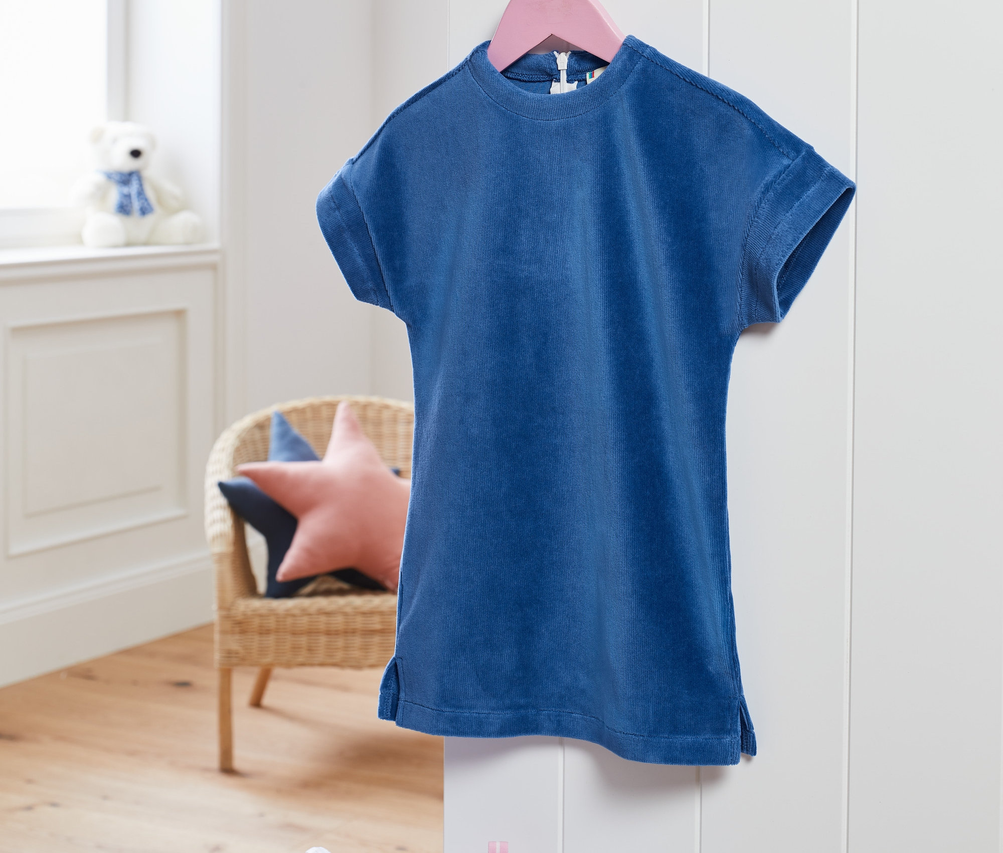 Modré strečové manšestrové šaty visí na růžovém ramínku.