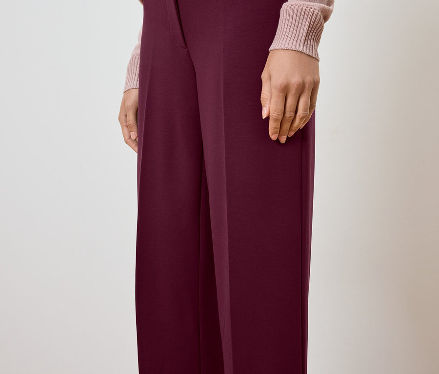 Částečný pohled na osobu nosící vínové kalhoty a světle růžový svetr.