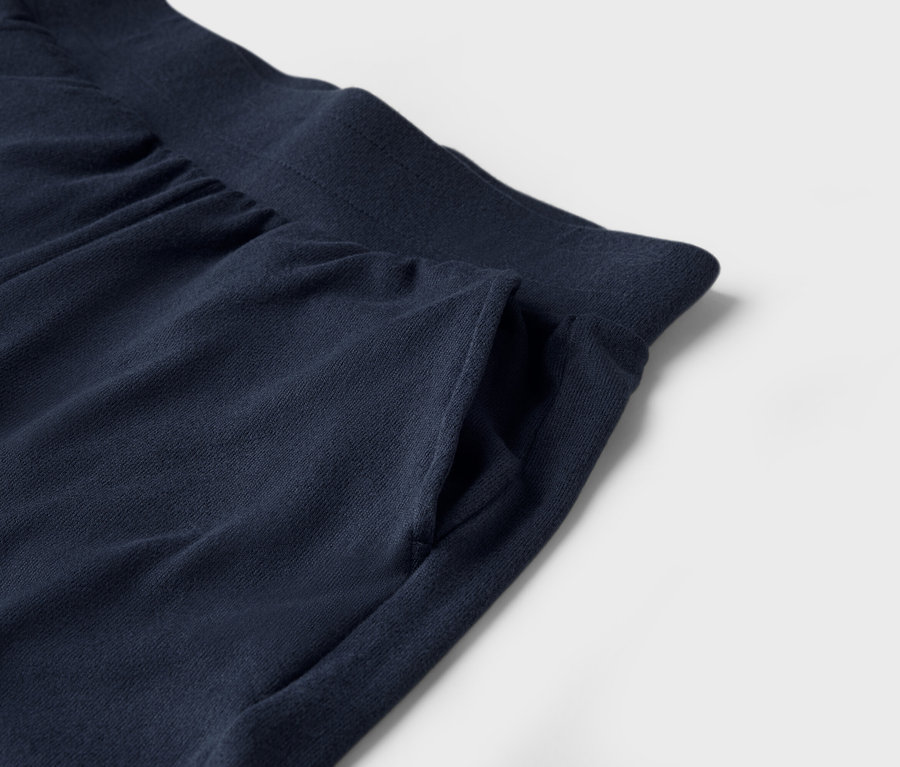 Detail tmavě modrých tepláků s kapsou na bílém pozadí.