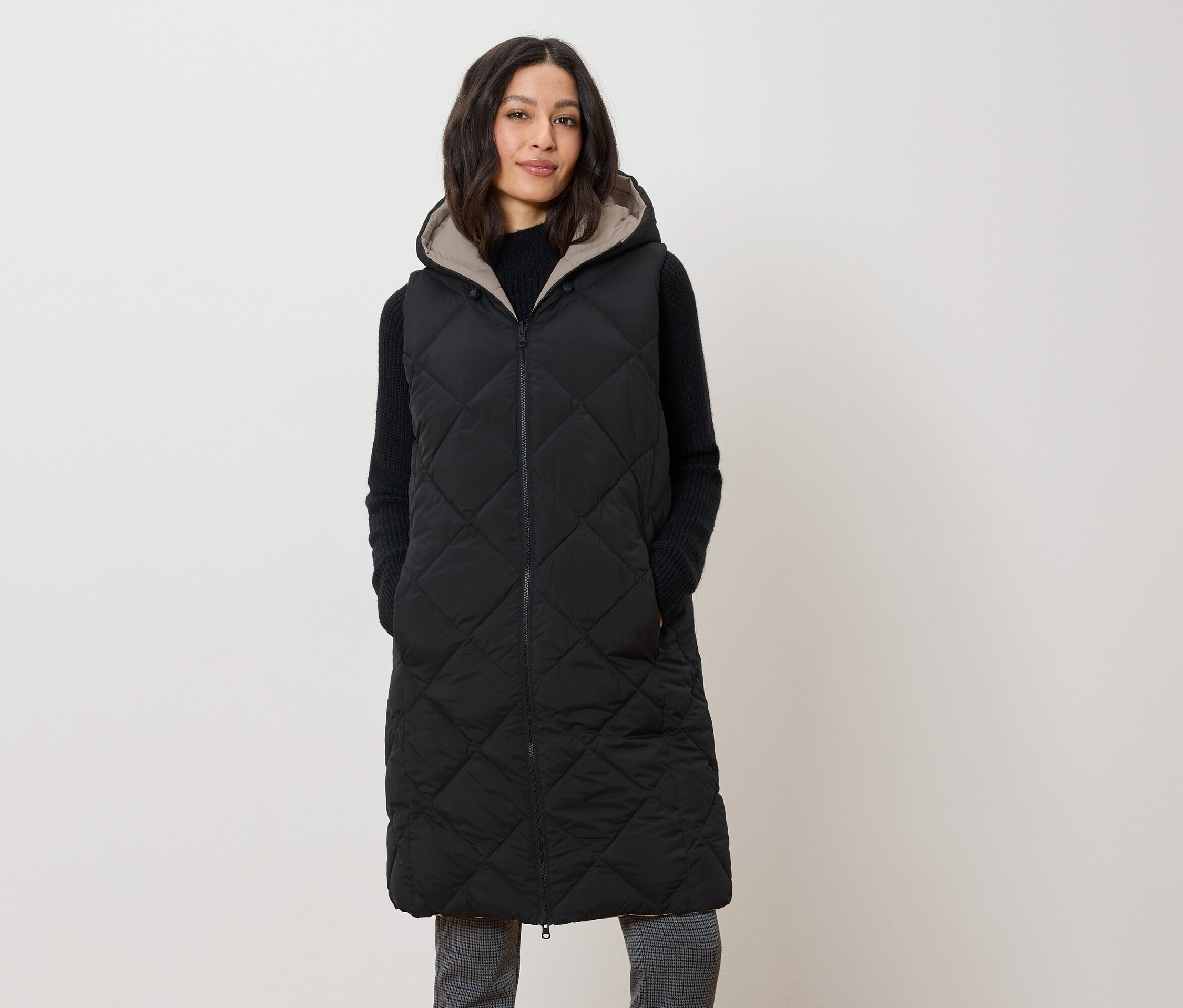 Žena má na sobě dlouhou prošívanou černou vestu s kapucí.