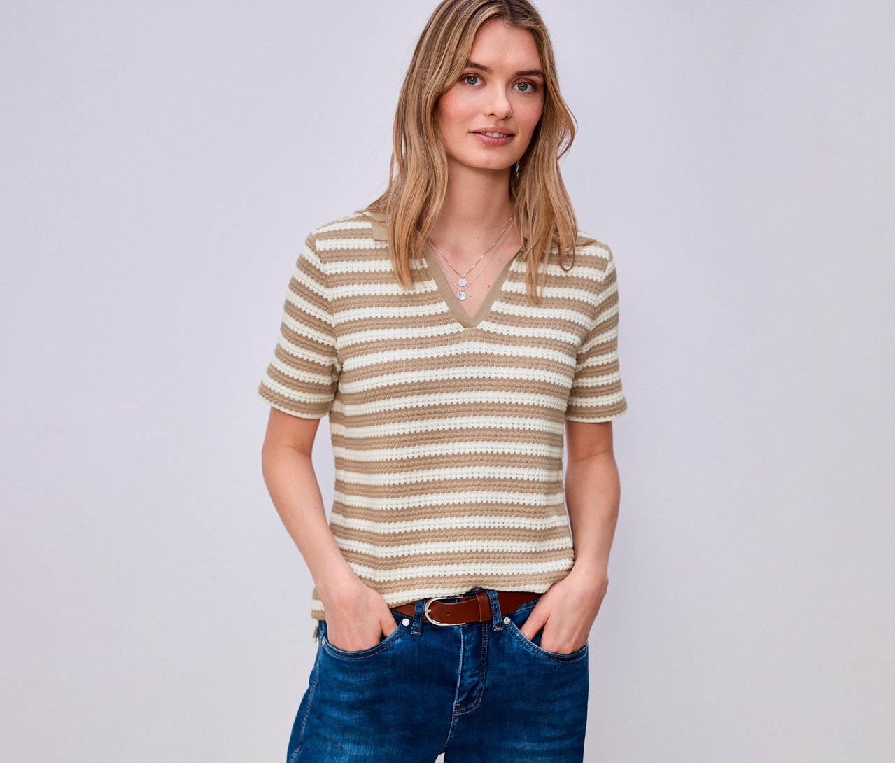 Žena v džínách a hnědém opasku má na sobě proužkované úpletové tričko Street One s výstřihem do V.