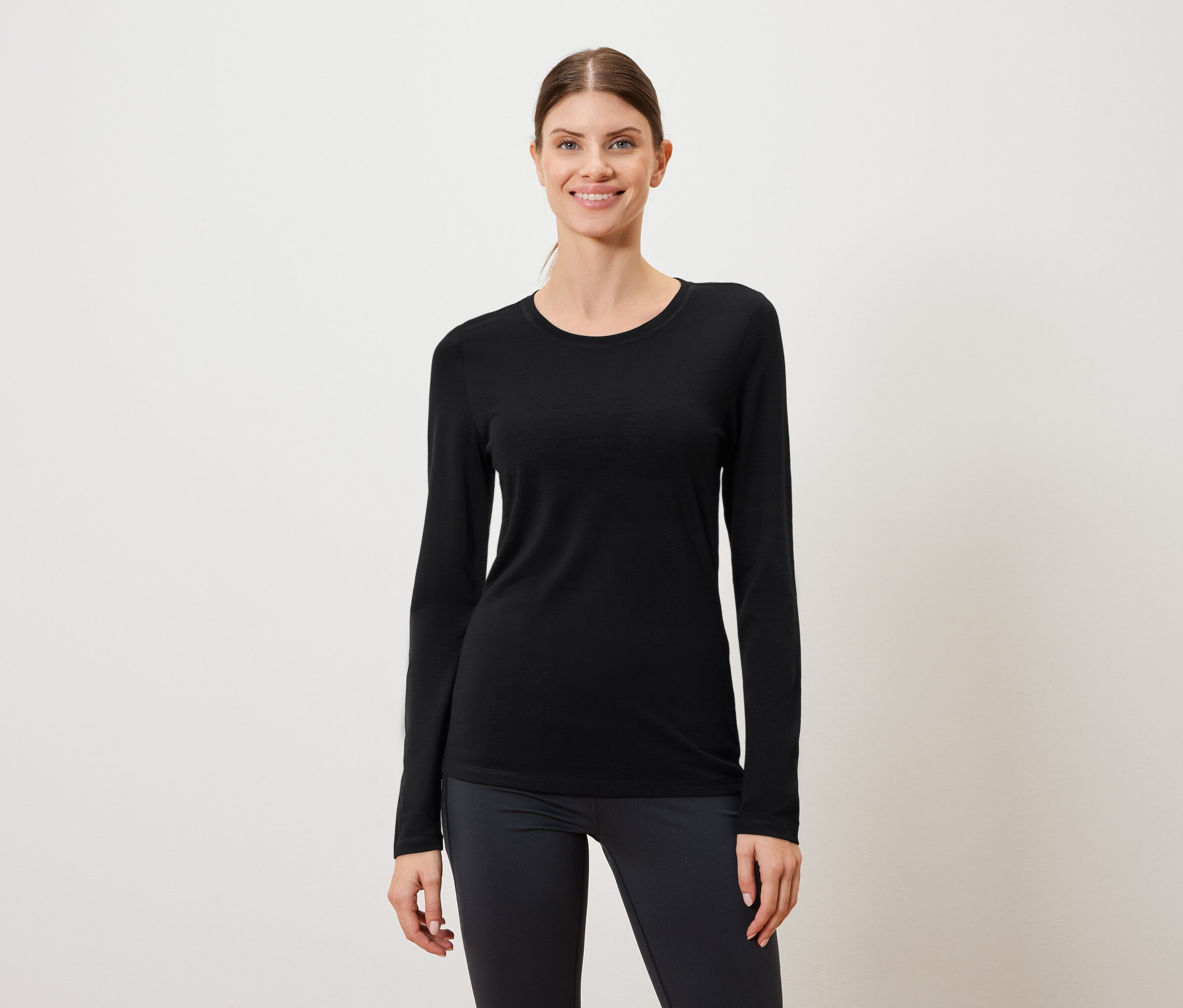 Žena má na sobě černé tričko s dlouhým rukávem a tmavé legíny na bílém pozadí.