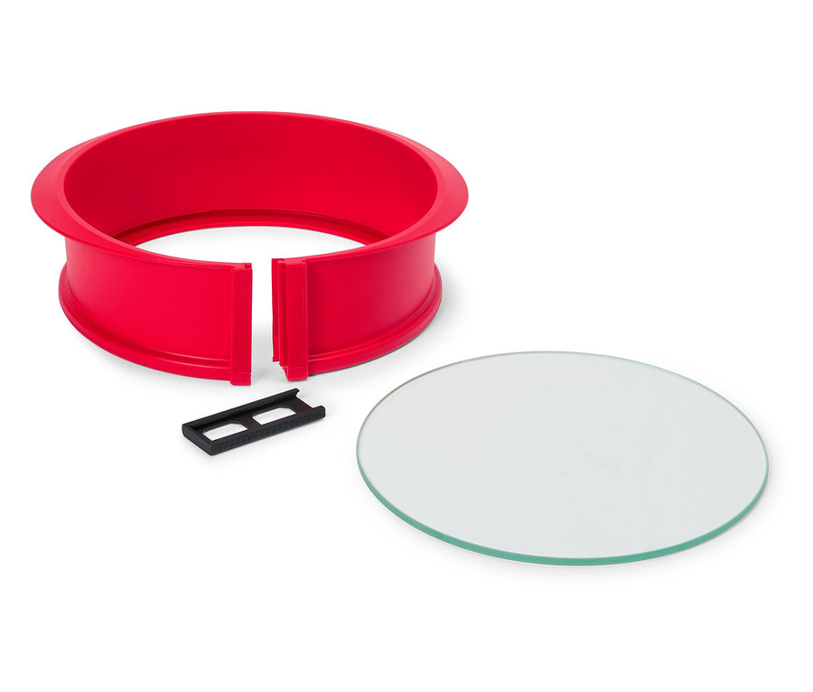 Červený kulatý dortový rám s černým klipem a kulatou skleněnou deskou na bílém pozadí.